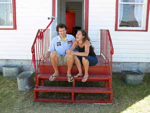 Kuva Kylesta valkoisen talonsa rappusilla. Talossa on punaiset ikkunanpuitteet.