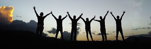 Ryhmä nuoria seisoo kädet ylhäällä yhteen liitettyinä auringonlaskussa. Heidät on kuvattu vastavaloon niin, että he erottuvat siluetteina.